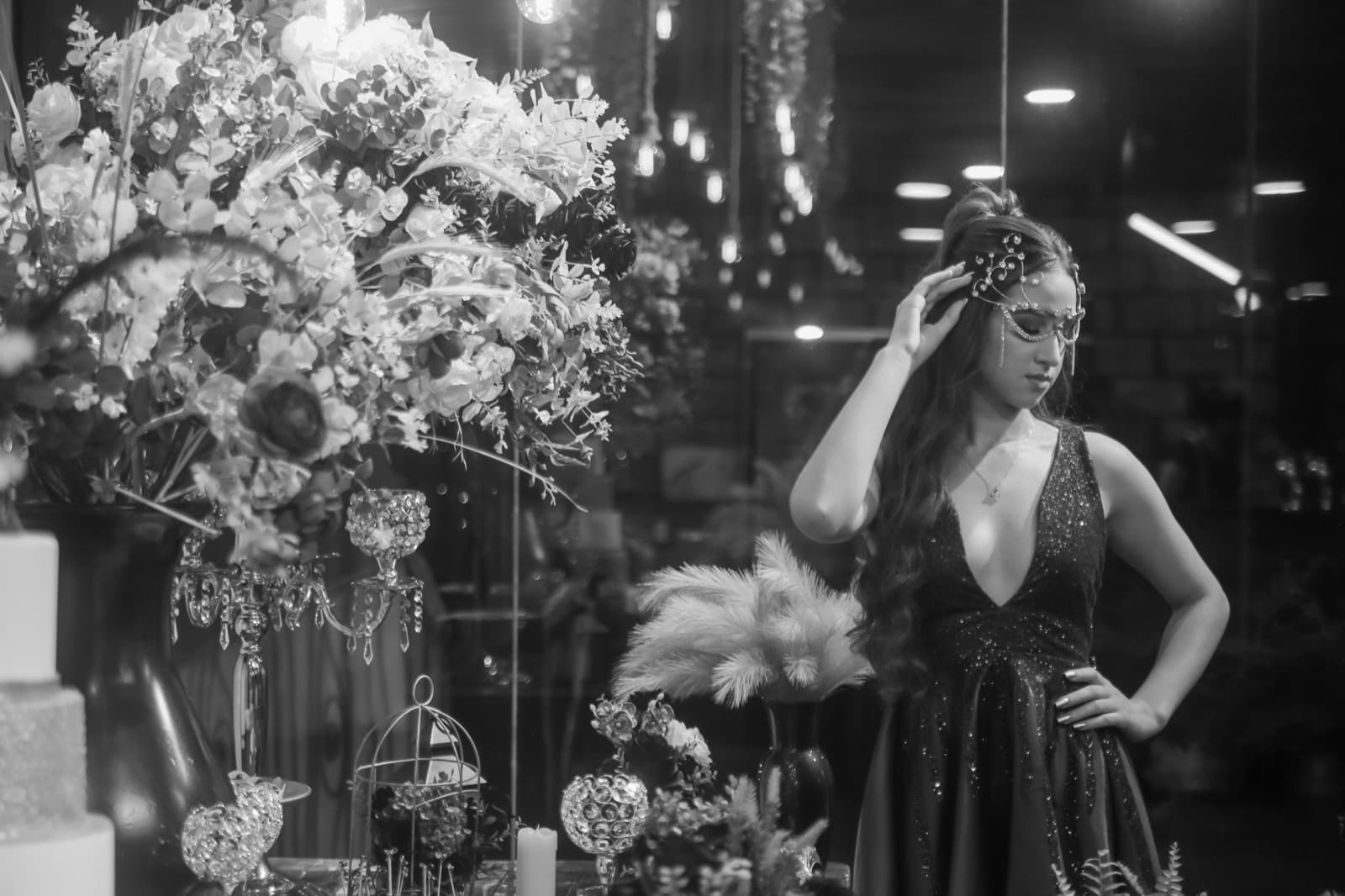 Debutante com máscara de cristais ao lado dos arranjos de flores, em preto e branco