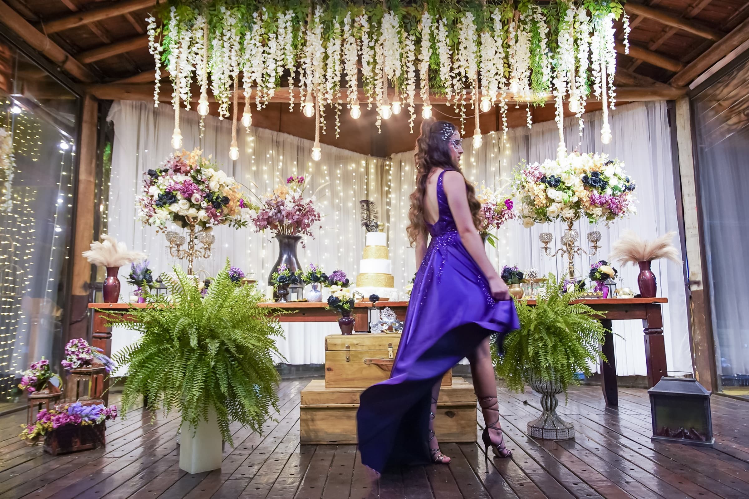 Debutante de vestido roxo diante da mesa do bolo decorada, no Fazenda Santa Isabel Premium