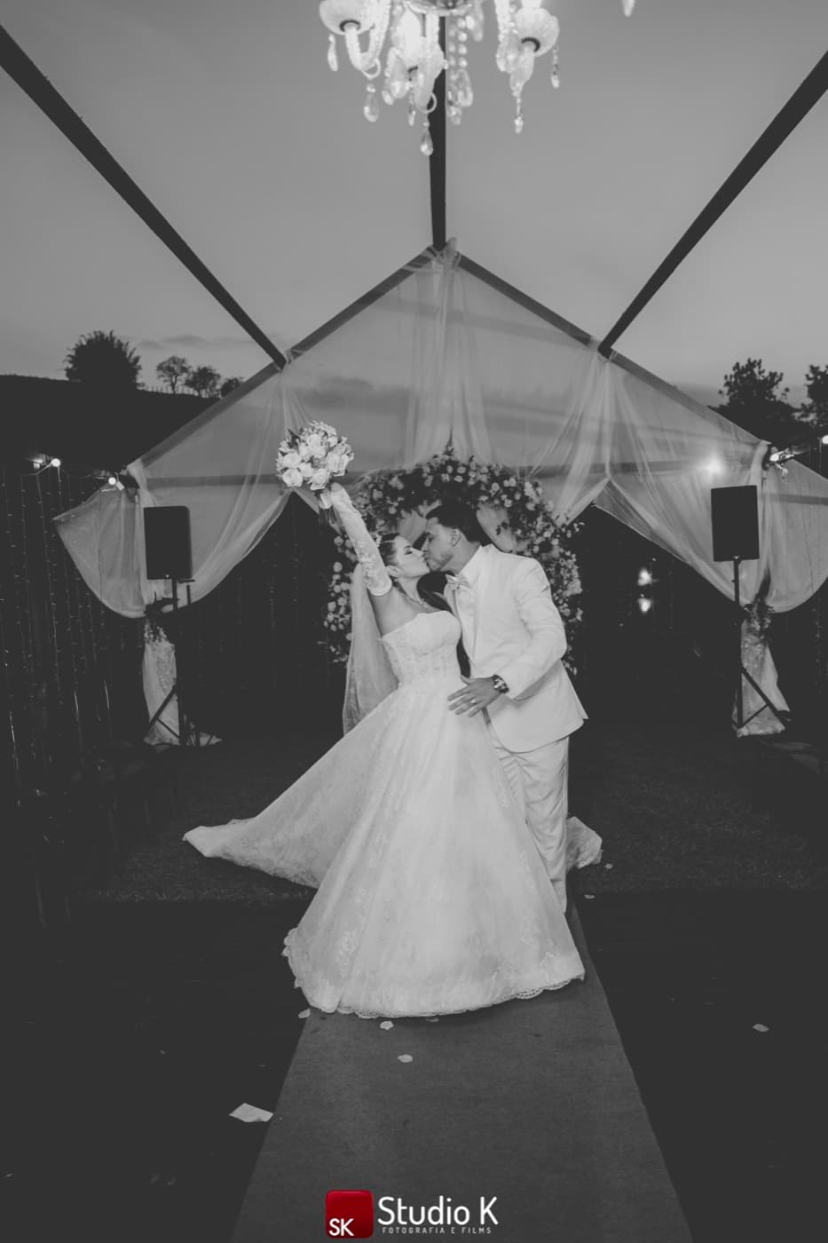 Noivos se beijando no altar ao entardecer, sob o lustre de cristal