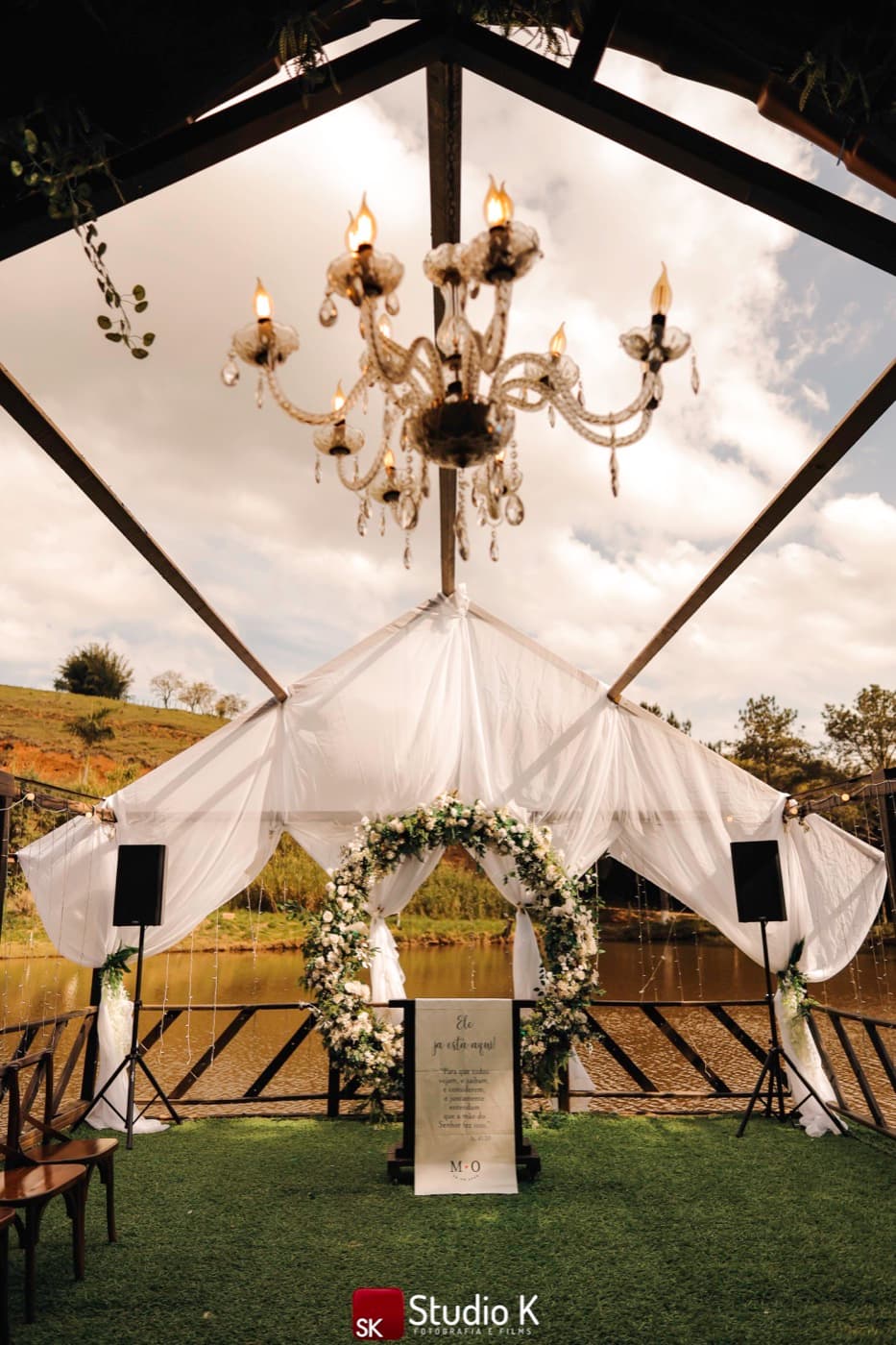 Gazebo da cerimônia à beira do lago, com lustre de cristal e arco de flores