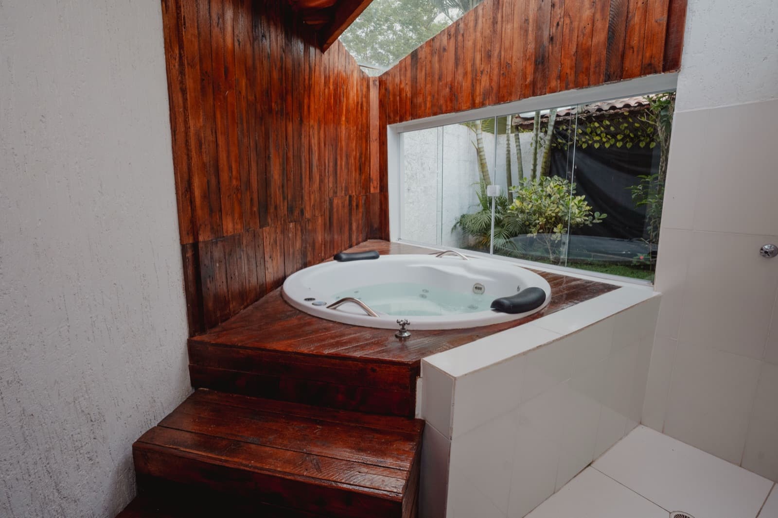 Banheira de hidromassagem da suíte, com parede de madeira e vista pro jardim