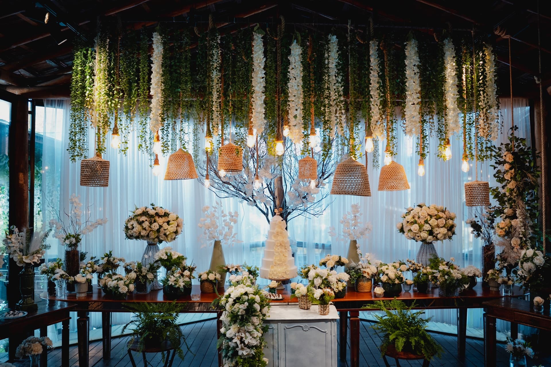 Mesa de doces completa de um casamento real, com bolo ao centro e luminárias de palha